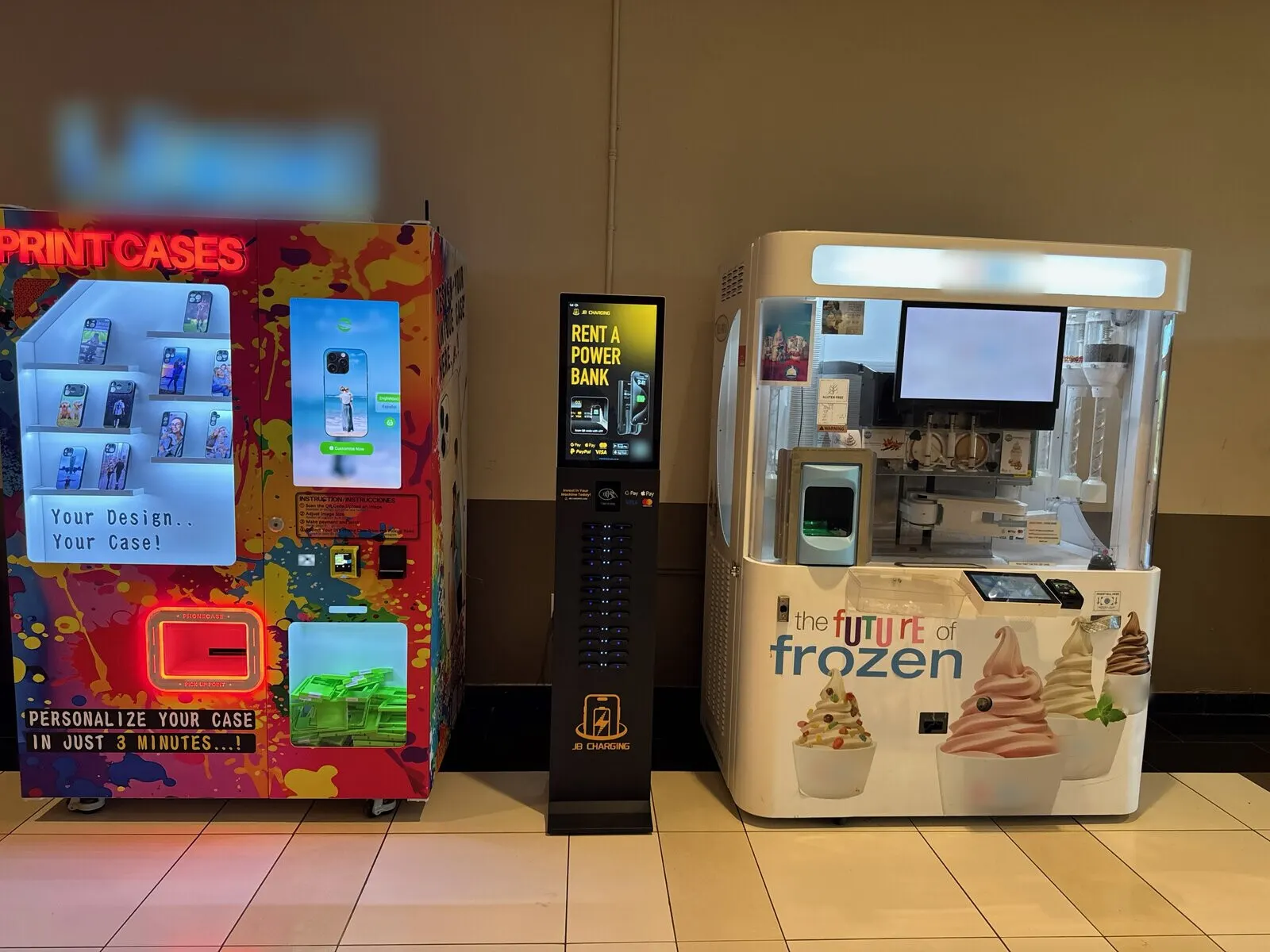 A JB Charging J24 Pro tower with a "Rent a power bank" screen, standing between two other self-service kiosks along an indoor corridor wall